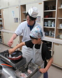 子供が講師と魚の揚げ焼きに挑戦する写真